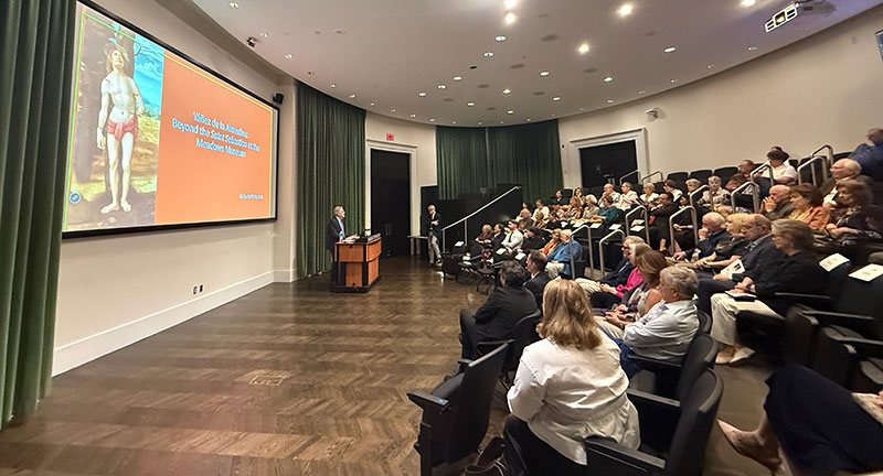 View of the Meadows auditoriium from the side with audience members looking towards a speaker at a podium in front of a screen