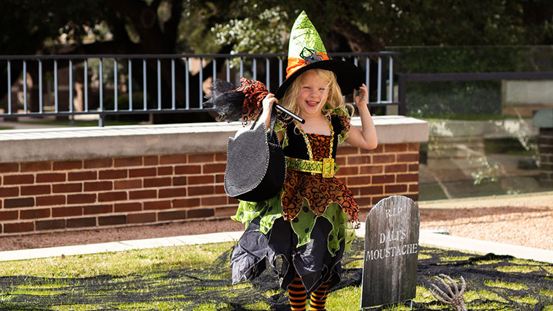 Little girl in Hallowe'en witch outfit carrying a broomstick